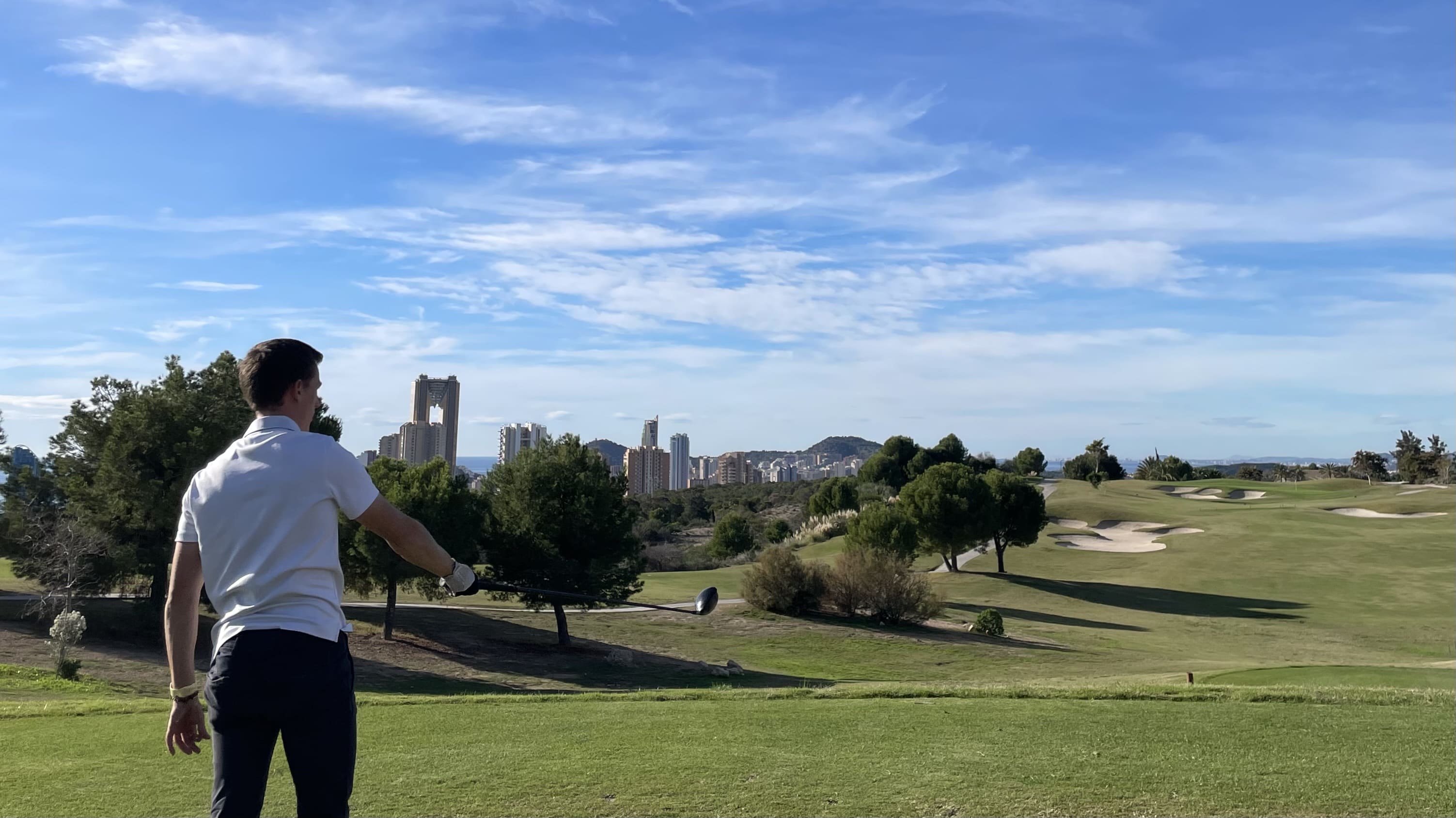 Golfista sosteniendo un driver en un campo de golf mediterráneo — banner de colecciones Skrambel de grips de golf